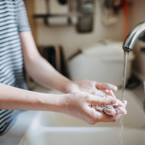Mikrobielle Risiken, Lebensmittelhygiene Person mit geringeltem T-Shirt im Anschnitt der linken Bildhälfte, die ihre Hände in einem Waschbecken mit Seife wäscht.