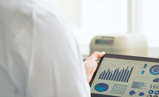 Analytik Tablet mit Diagrammen wird von zwei Personen im weißen Kittel gehalten.