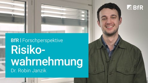 Porträtfoto von Dr. Robin Janzik (rechts im Bildbereich) vor weißer Wand. Links Fenster mit Blick auf gegenüberliegenden Teil des BfR-Gebäudes. Links unten im Bild türkisfarbene Textbox mit weißer Schrift mit Videotitel, oben rechts weißes BfR-Logo.