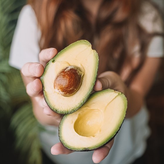 Ernährungsrisiken Frau hält aufgeschnittene Avocado in die Kamera. In einer Hälfte befindet sich noch der Kern.