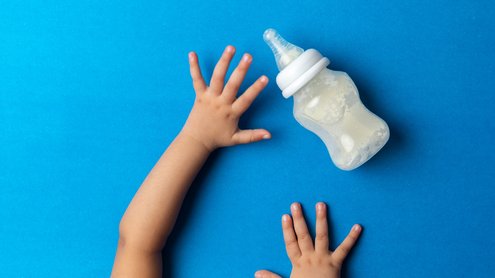 Auf der Abbildung sind Kinderhände und eine Milchflasche zu sehen